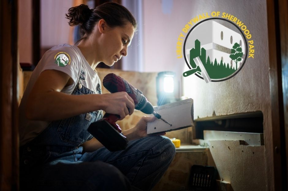 Drywall patch repair scene showing a woman kneeling in a dim workspace, holding a red power drill as she secures a small drywall piece illuminated by a work light. She is focused on the repair with tools around her. The residential project is near Sherwood Park, Edmonton, Alberta.