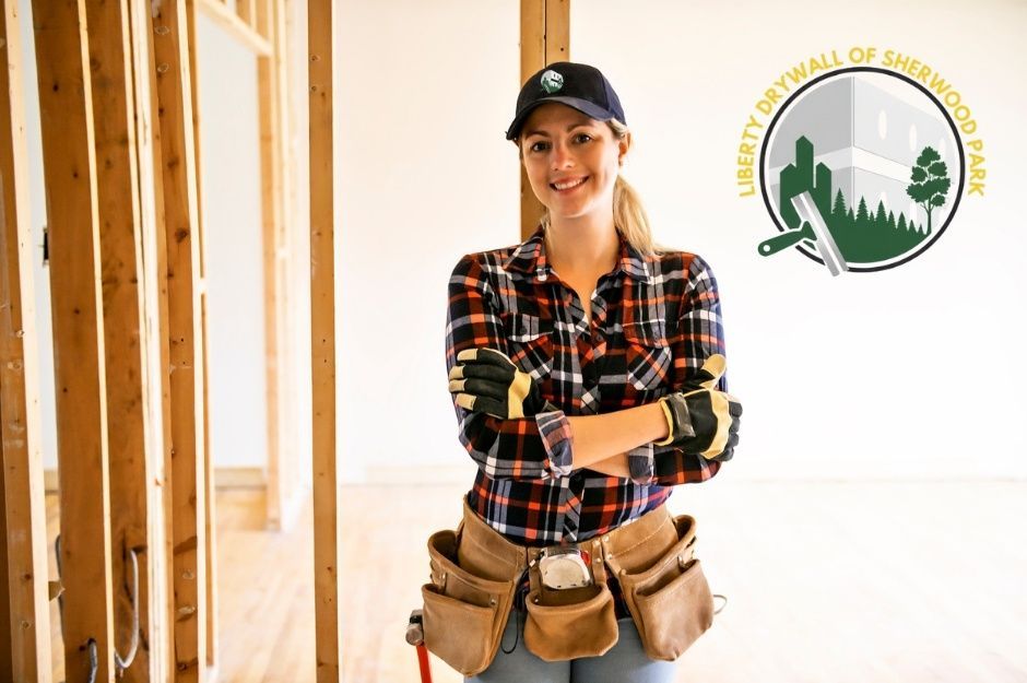A drywall repair company worker in a palid shirt smiles while standing standing confidently in a residential hallway with white walls and wooden framing near 50 St, and 50 Ave, Calmar, AB.