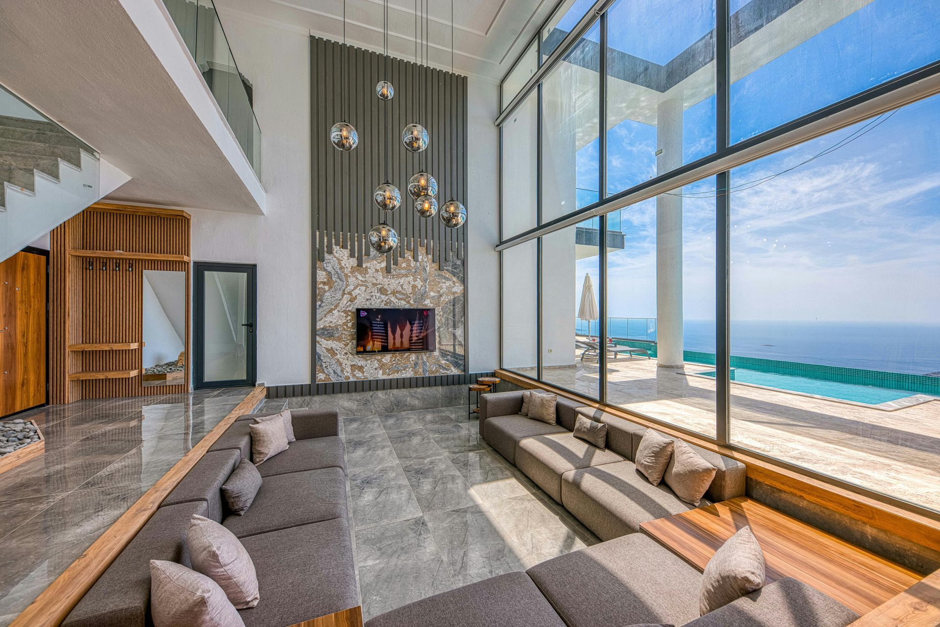Luxury living room with large windows overlooking the ocean; gray sofa, modern fireplace.