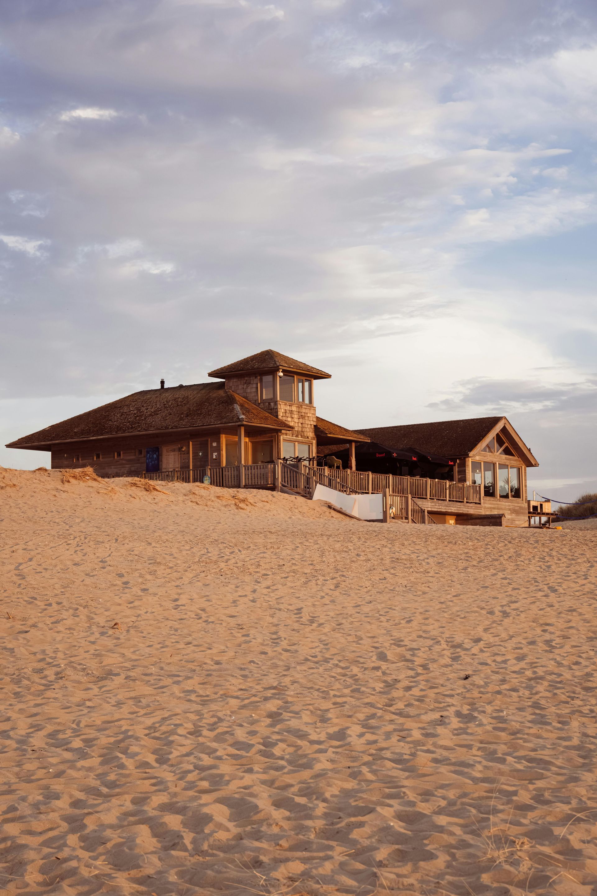 Beach house with weathered wood siding on a sandy dune, under a cloudy sky.