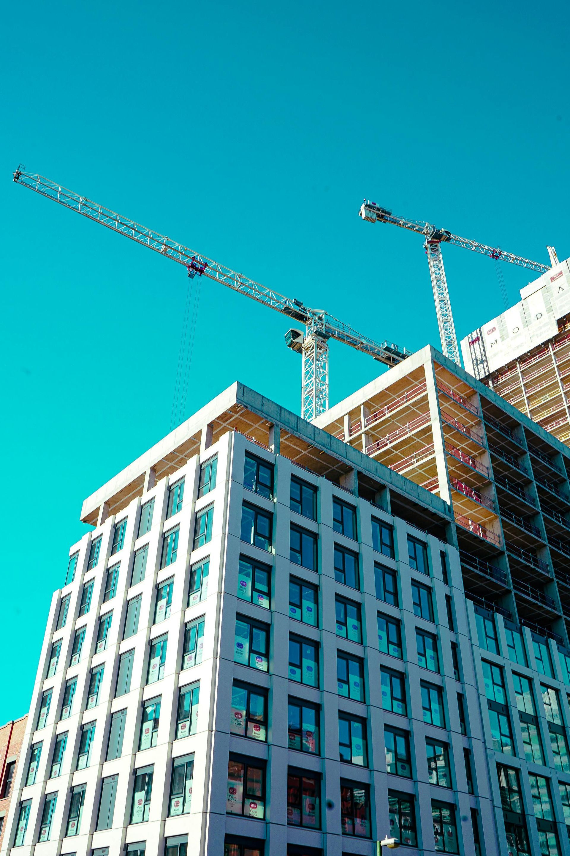 High-rise building under construction with two cranes against a bright blue sky