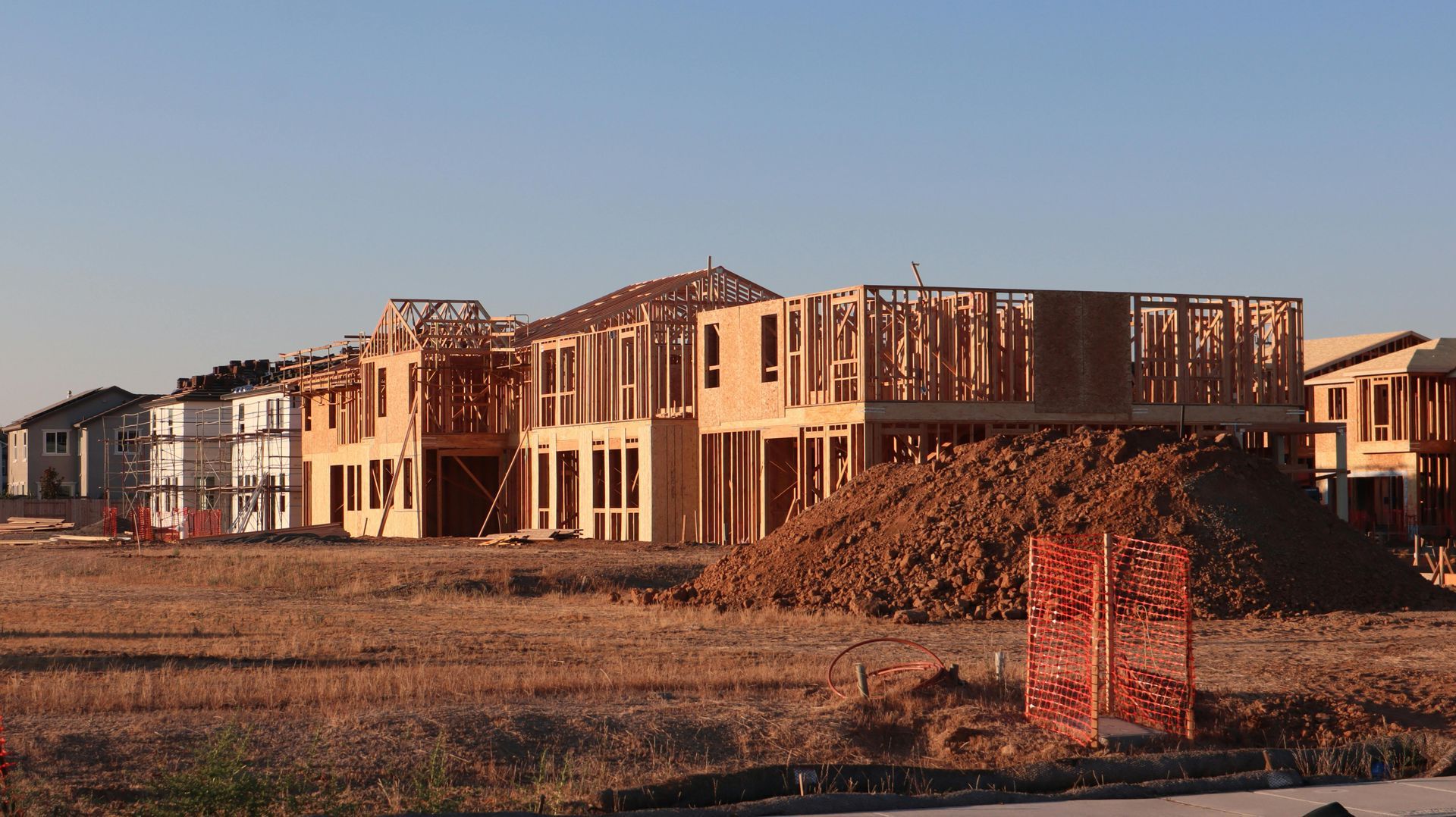 Partially built houses at a construction site with dirt piles in the foreground at sunset