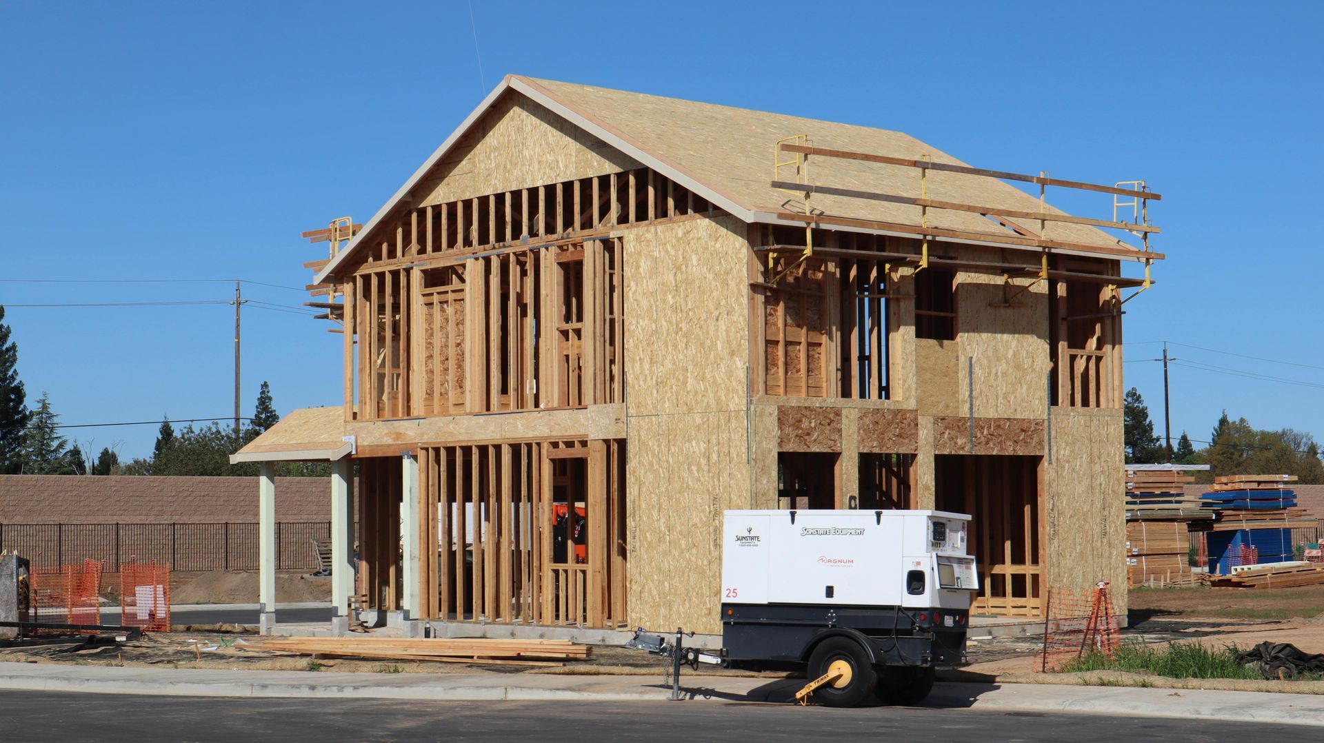 Partially built wooden house framing on a construction site with a white trailer in front