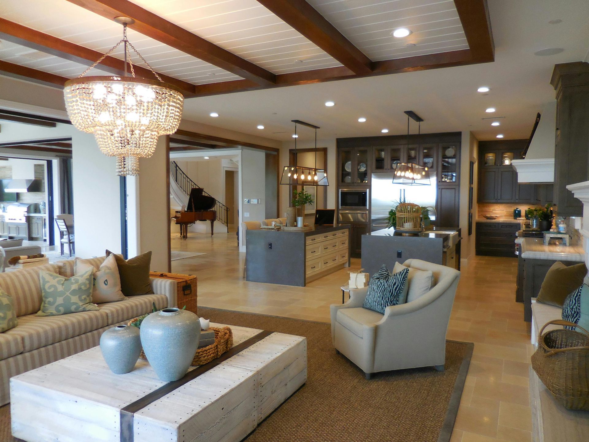 Bright open living room with beige sofa, armchair, coffee table, chandelier, and kitchen in the background
