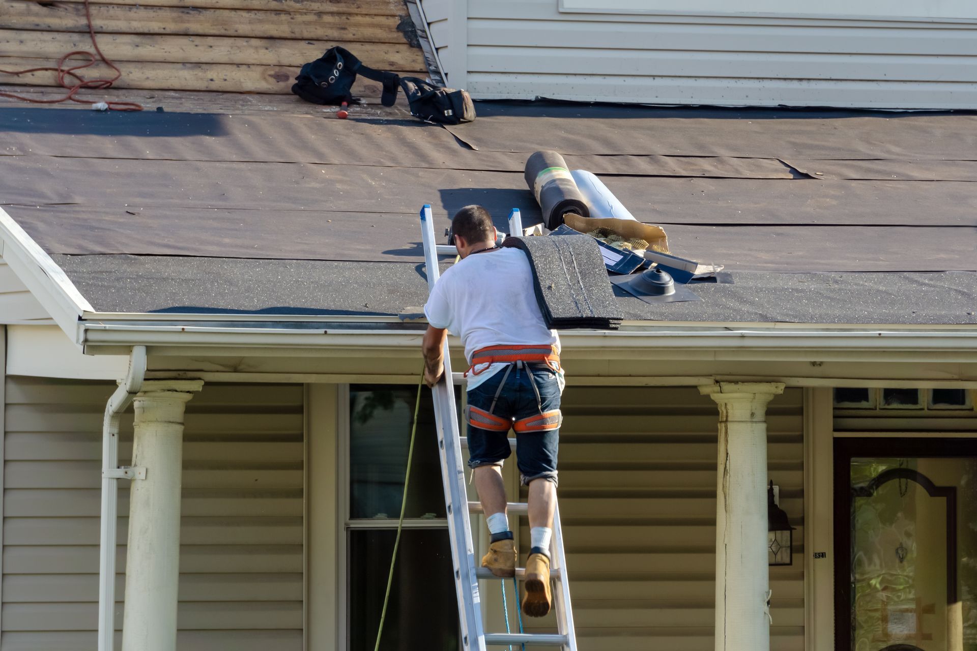 Roofer on ladder removing old shingles and installing underlayment.