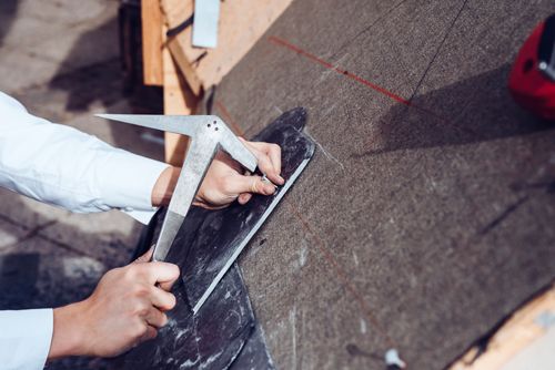 A roof repair contractor measuring shingles with a square tool during detailed roofing restoration.