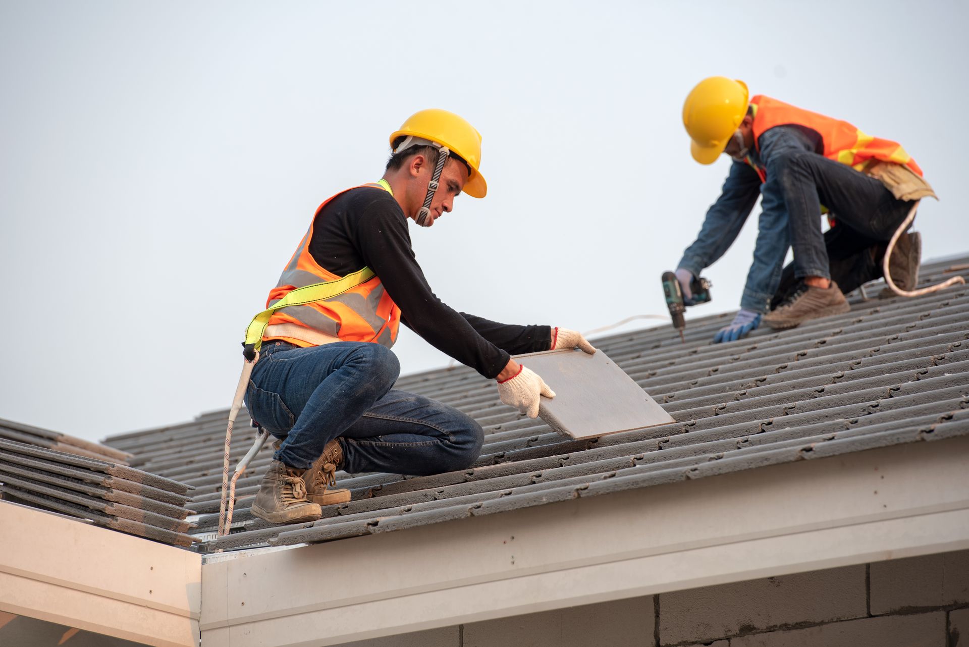 Two roofers using a drill to install roof tiles during a roofing replacement on a building.