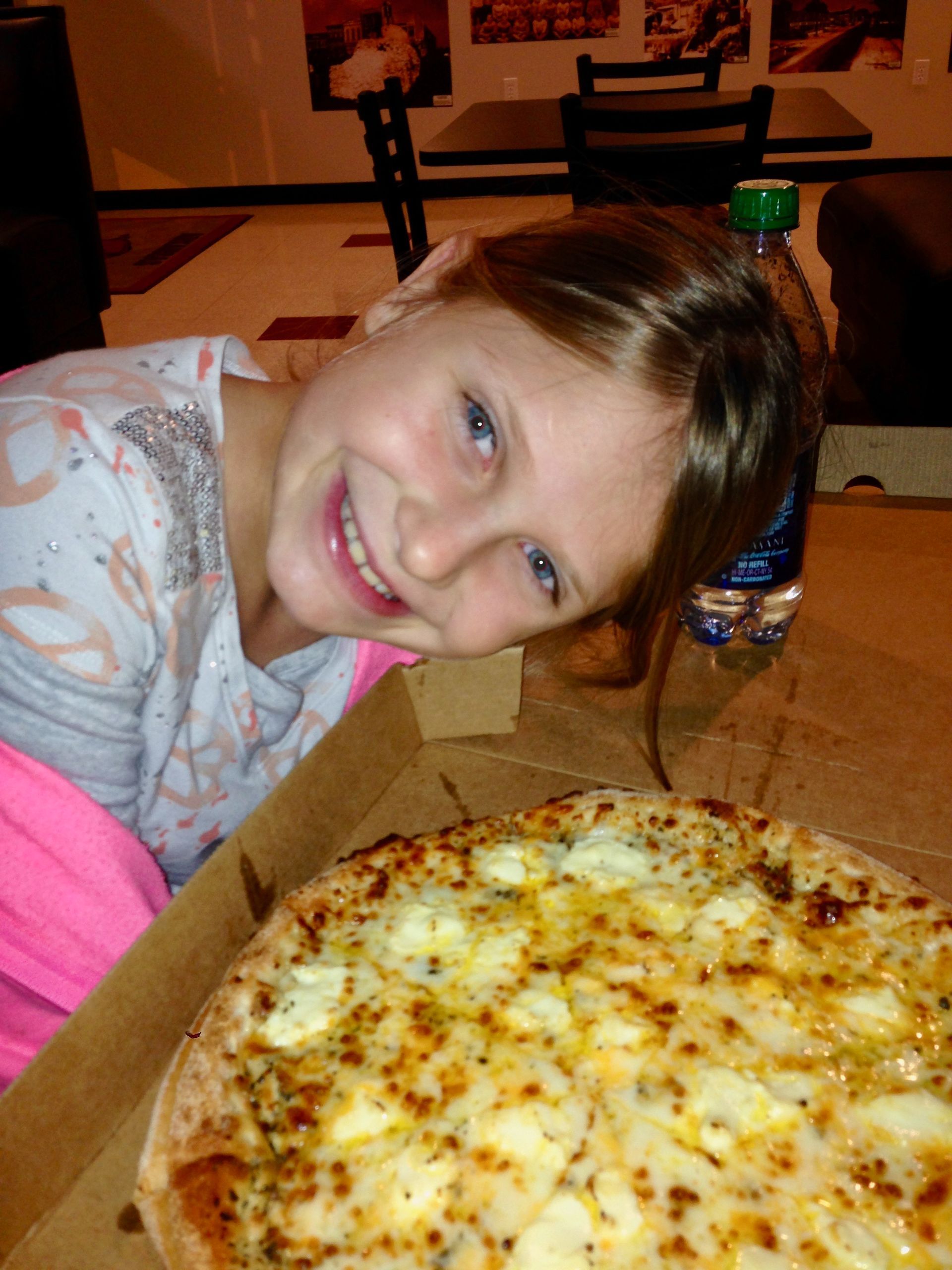A little girl is sitting next to a pizza in a box.