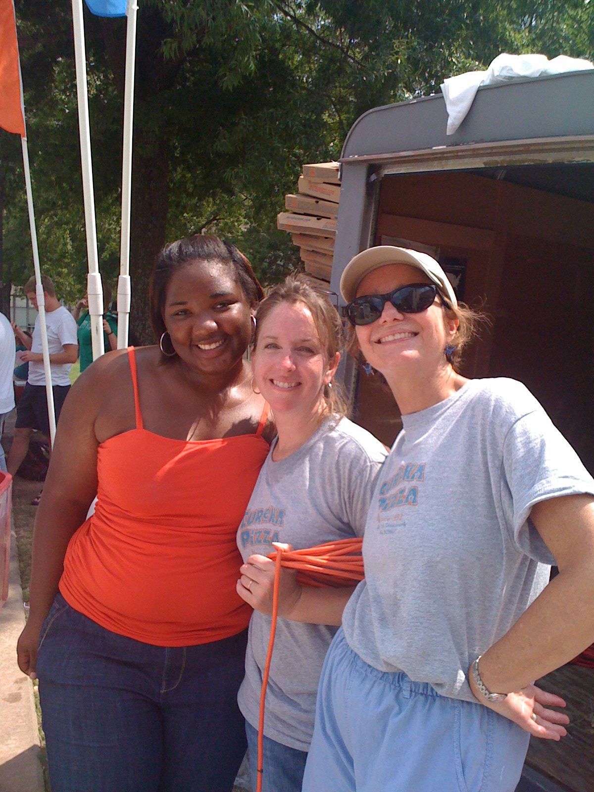 Three women posing for a picture with one wearing an orange tank top