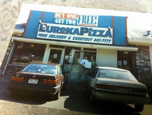 Two cars are parked in front of a restaurant called eurekapizza