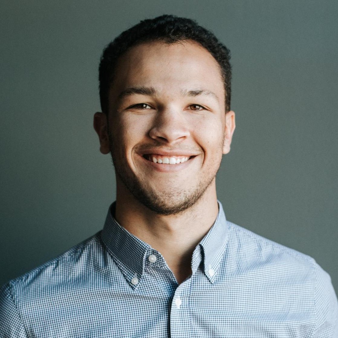 Professional headshot of a man against a grey background wearing a light blue shirt