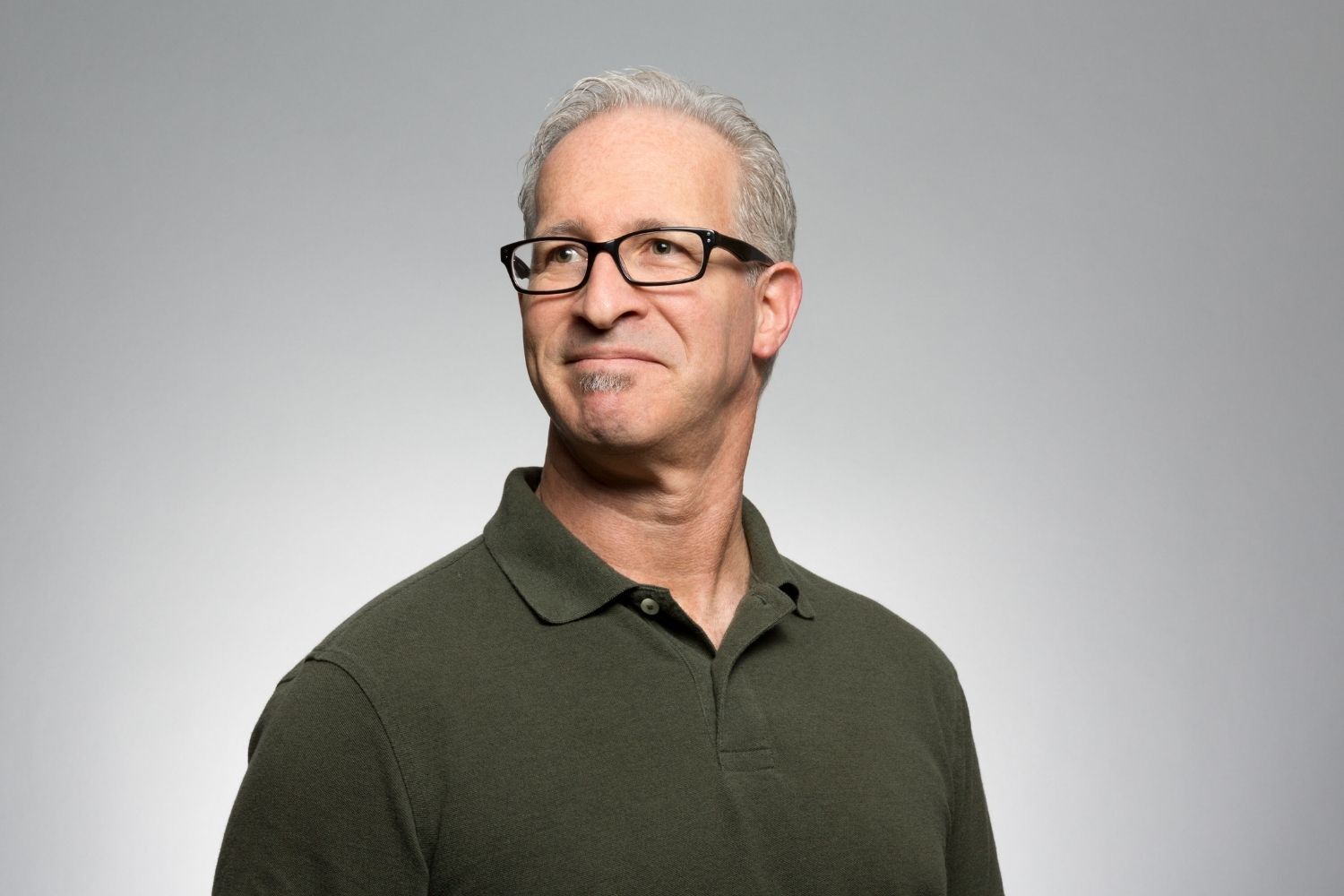 Professional headshot of a a gentleman looking outwards to the left, wearing glasses and a brown shirt