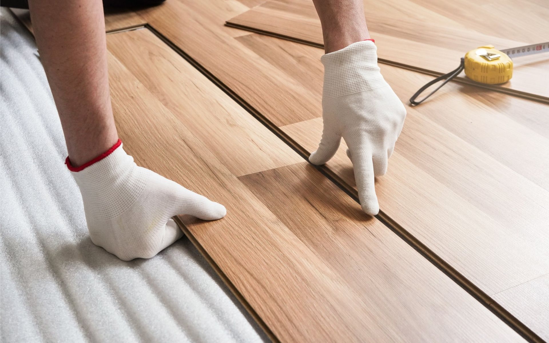 Person in gloves installing wooden floor planks.