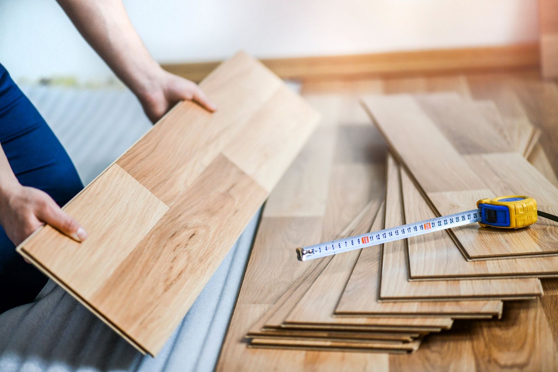 Person installing wood flooring with a measuring tape, indoors.