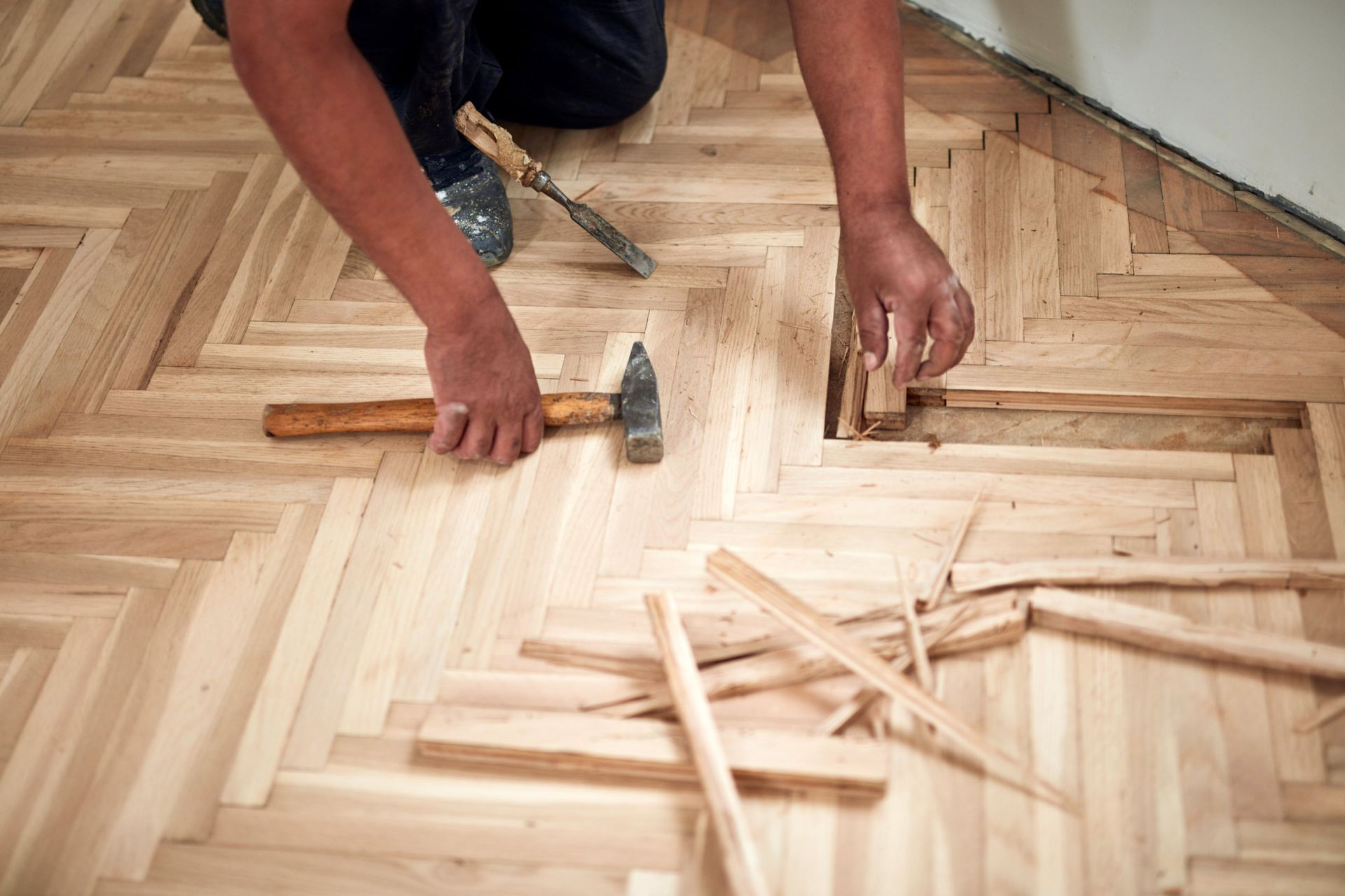 Person repairing a parquet wood floor with a hammer and chisel.