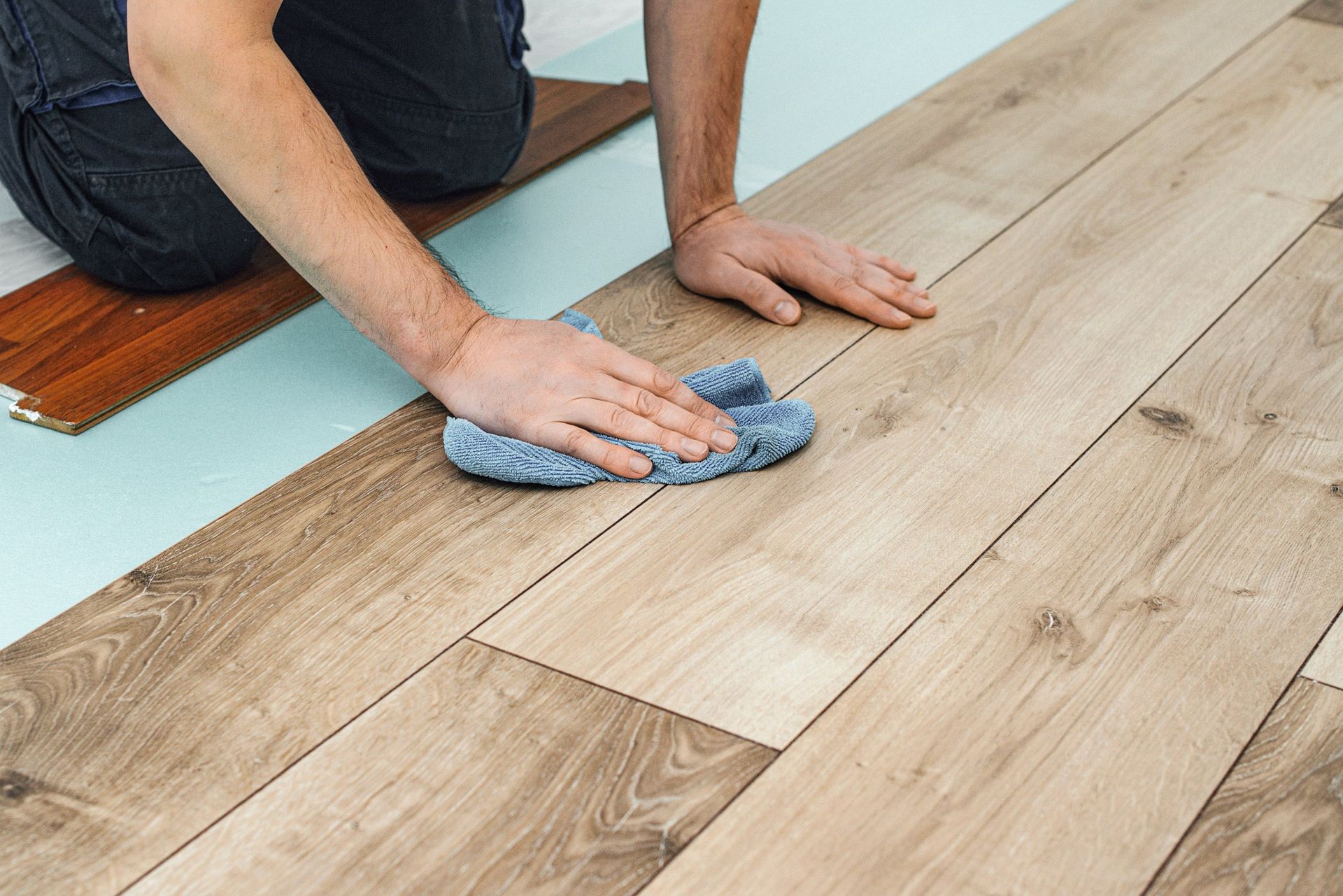 Person installing laminate flooring, wiping surface with a blue cloth, in a home.