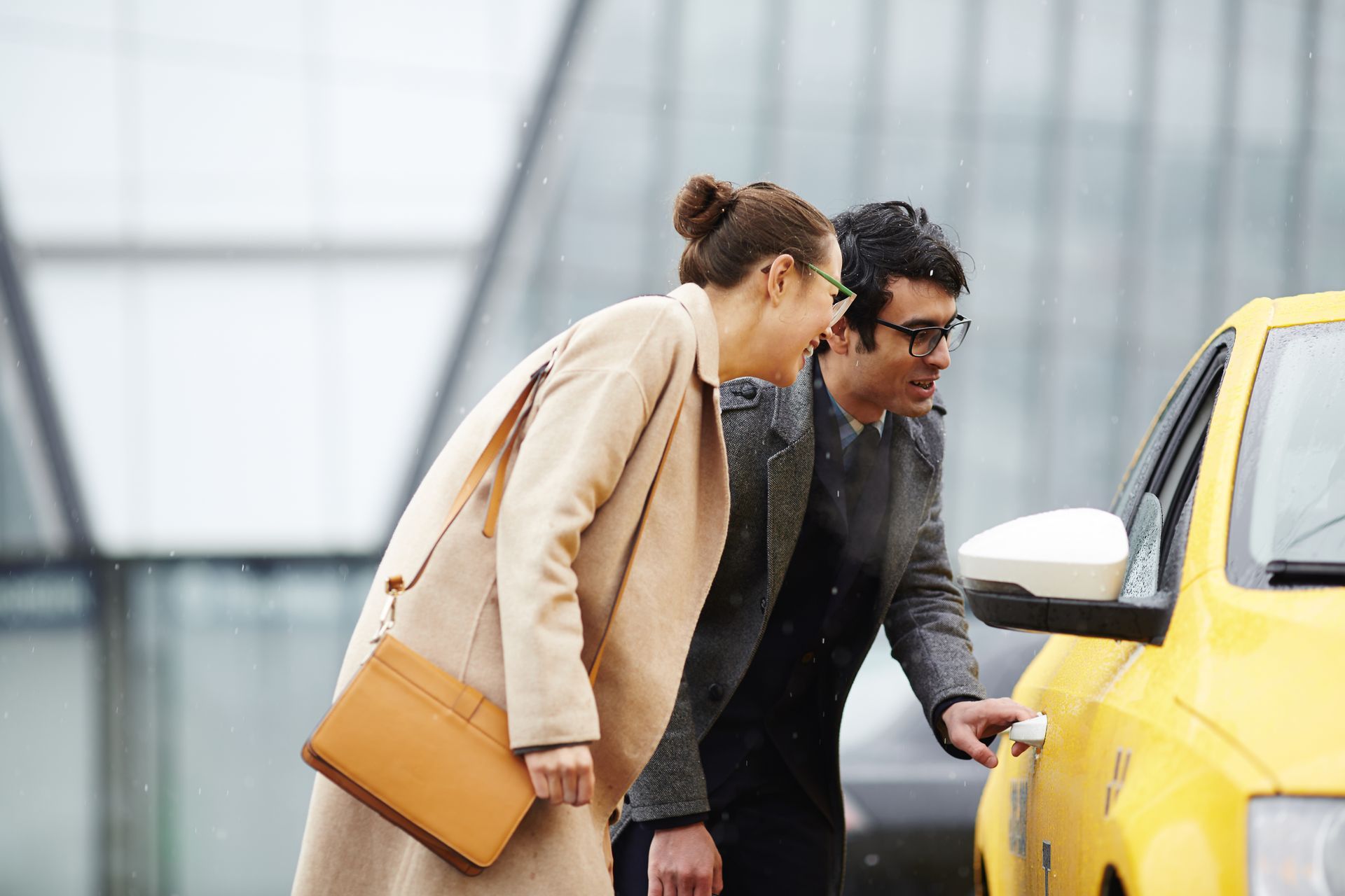 Woman and man opening a taxi door. Man holds door handle. Building in background.