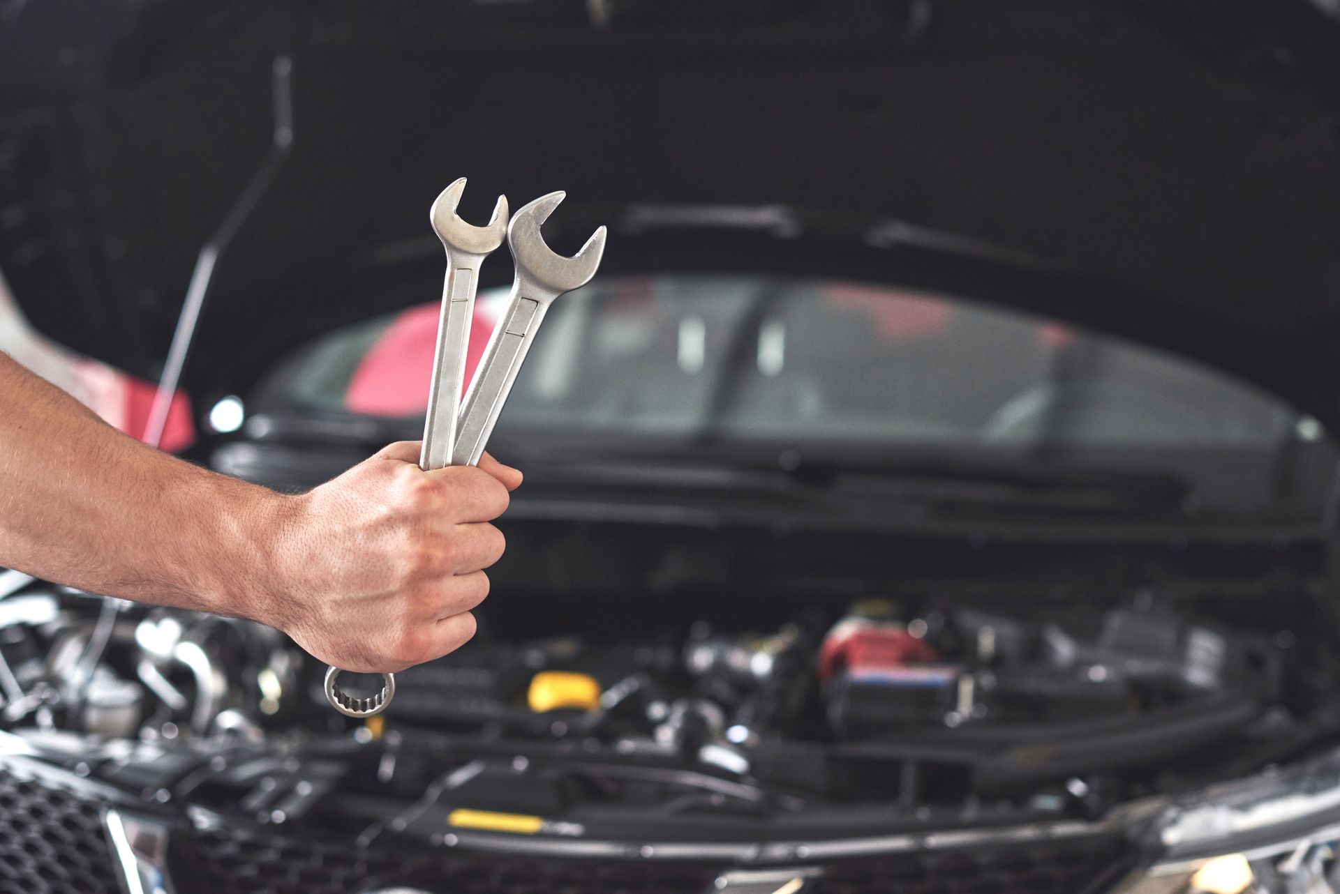 Mechanic holding wrenches, working on a car engine with the hood open.