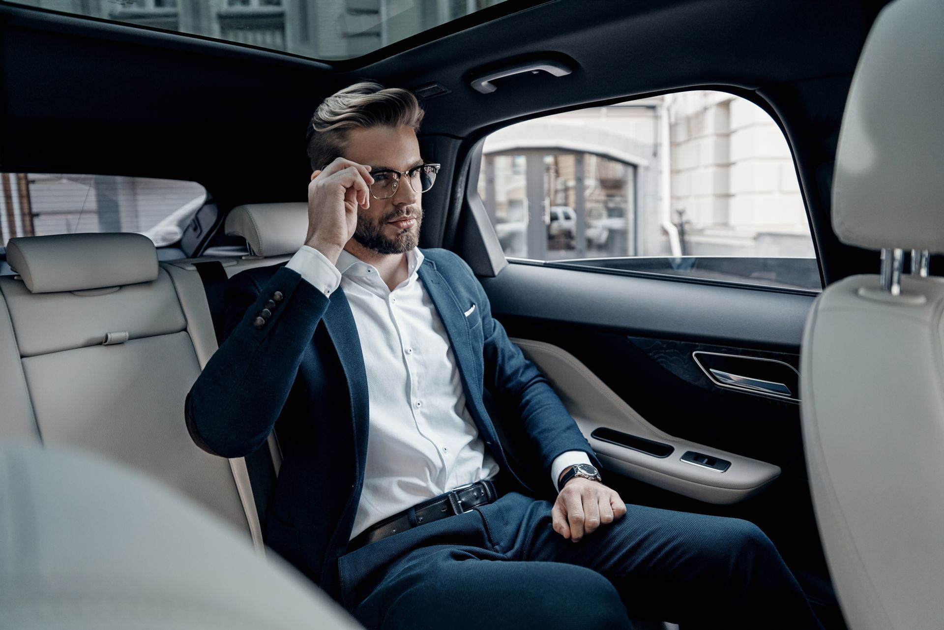 A man in a suit is sitting in the back seat of a car talking on a cell phone.