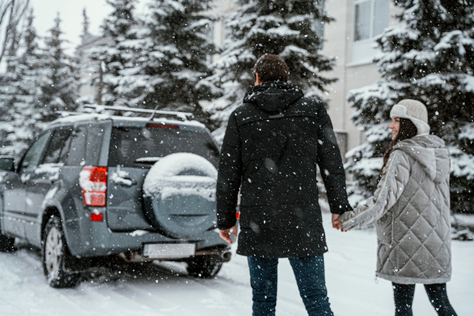 A couple, holding hands, walks toward a car in a snowy winter scene.