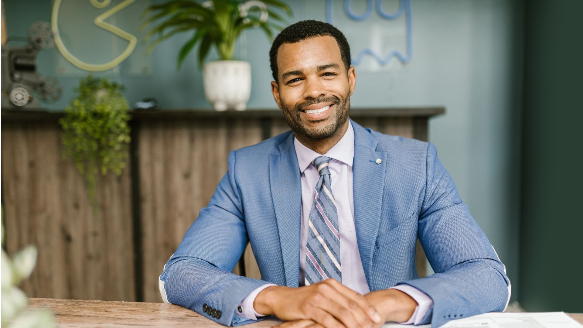 Smiling man in a blue suit seated at a table in an office setting