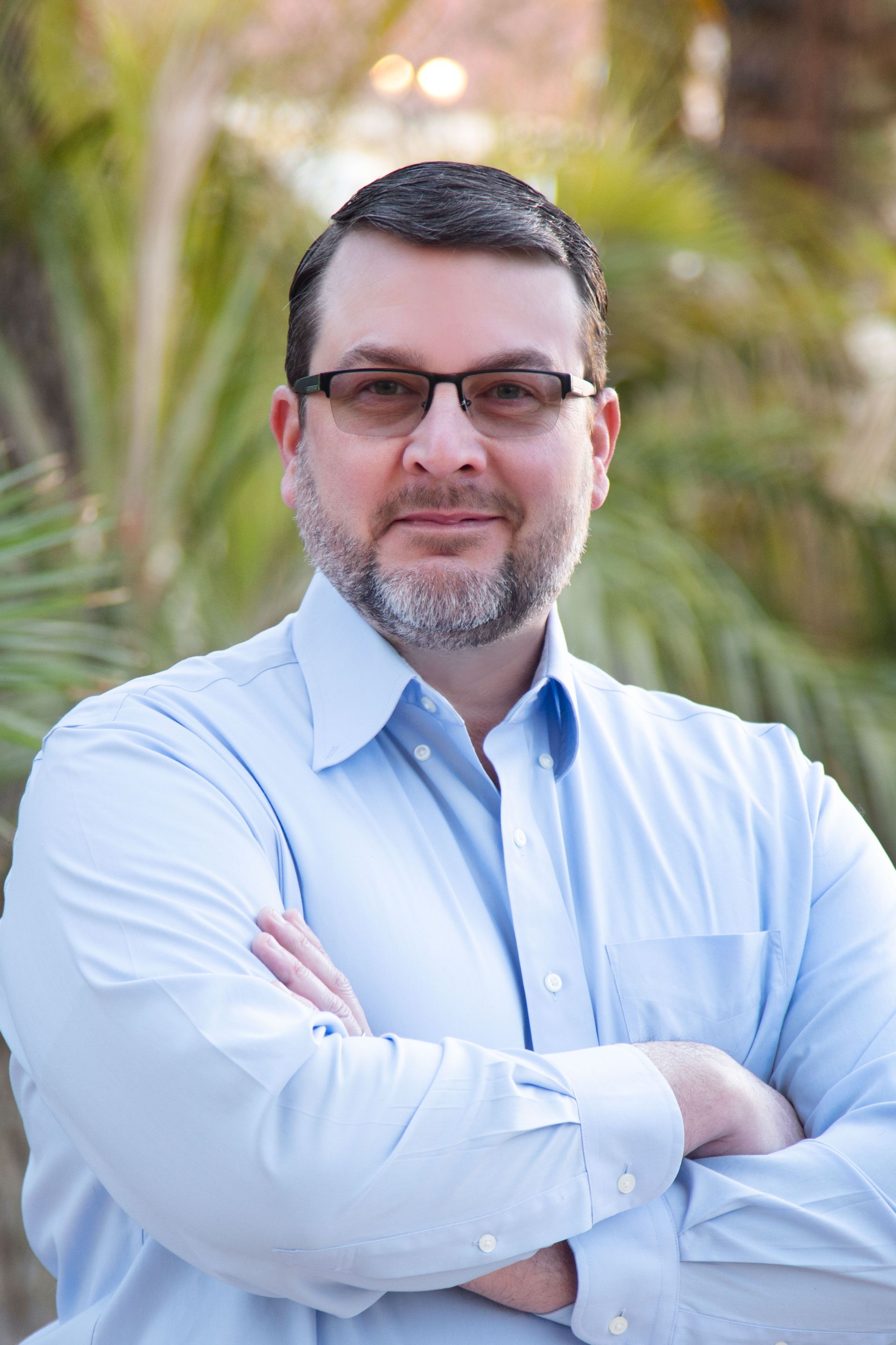 A man with glasses and a beard is standing with his arms crossed.