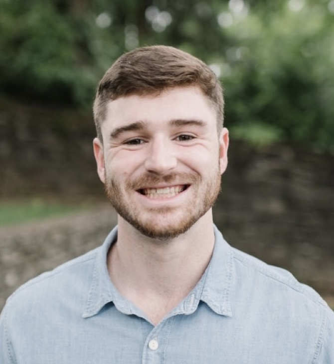 A man with glasses and a beard is standing with his arms crossed.