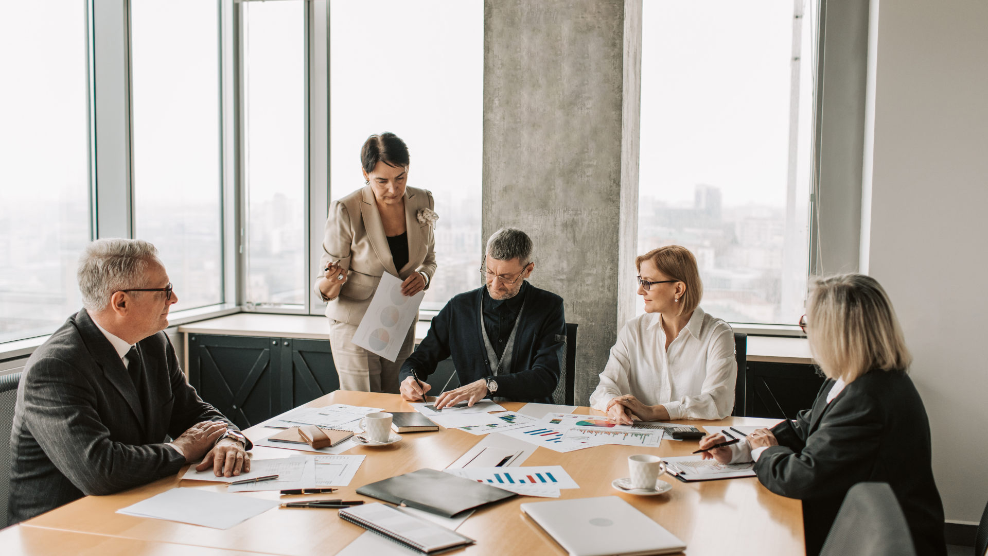 Businesspeople in a meeting around a table, reviewing documents in an office setting.
