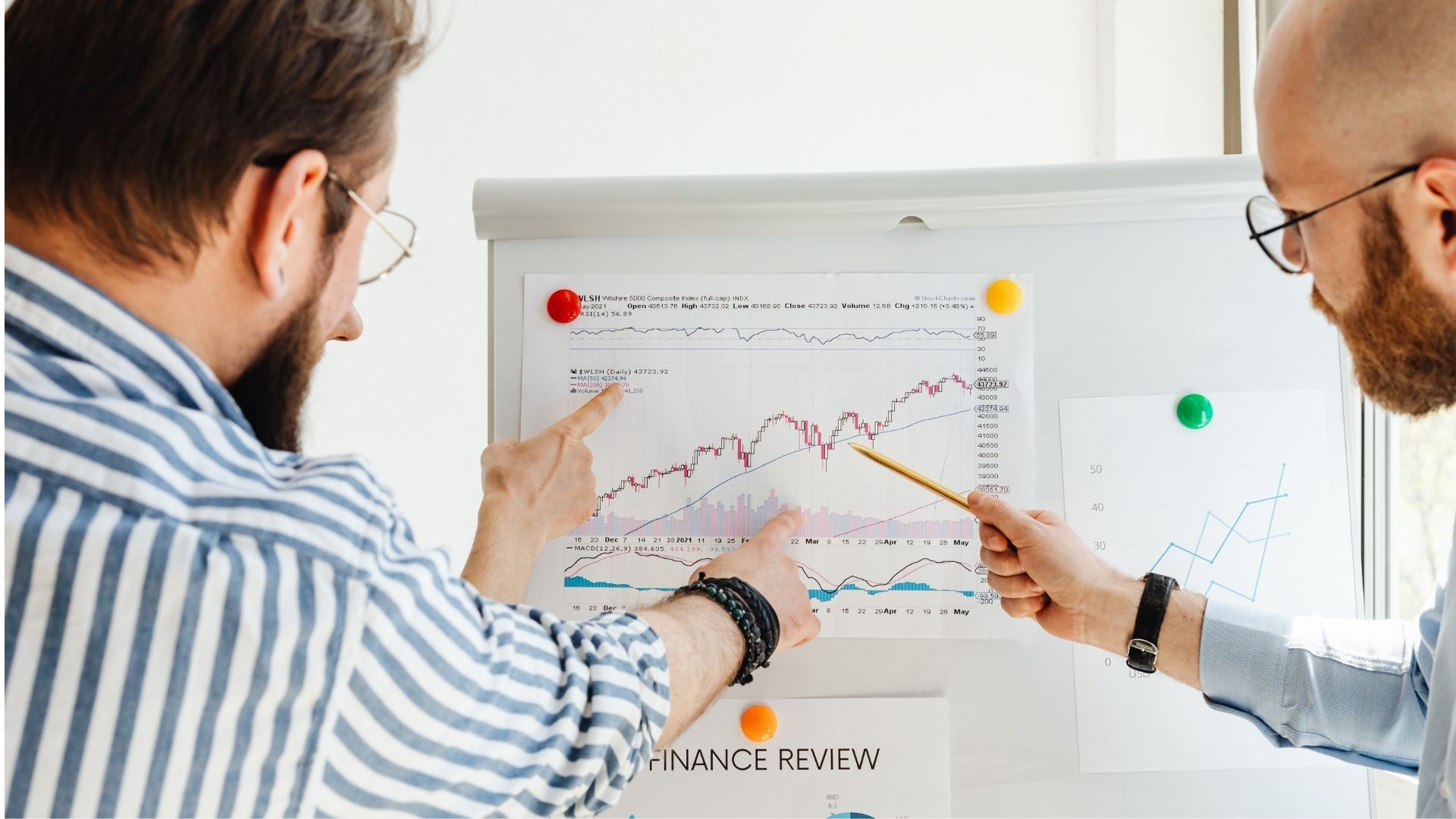 Two people point at a chart on a whiteboard in a bright office meeting.
