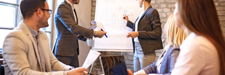 Business team in suits having a meeting, presenting on a whiteboard.