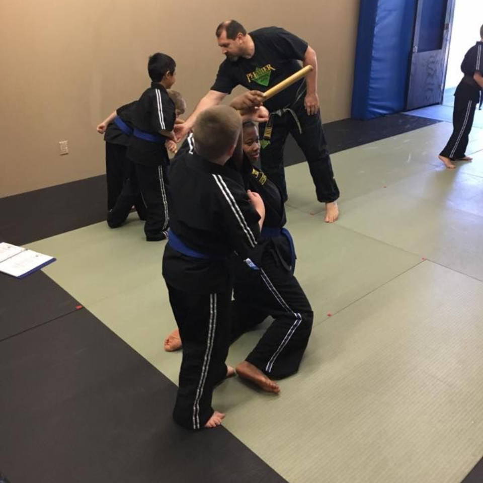 A group of children are practicing karate with a teacher in a gym.