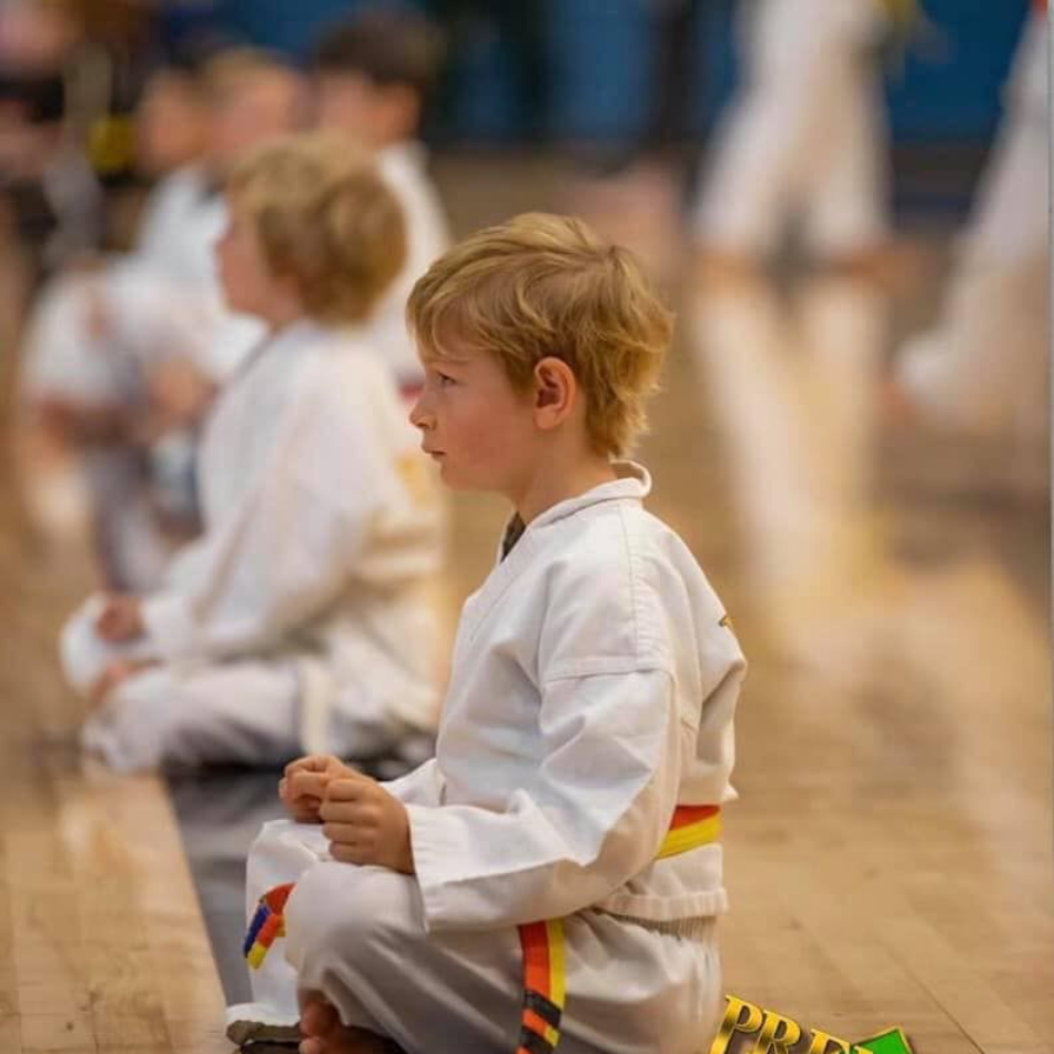 A man is kneeling down next to a young boy in a taekwondo class.
