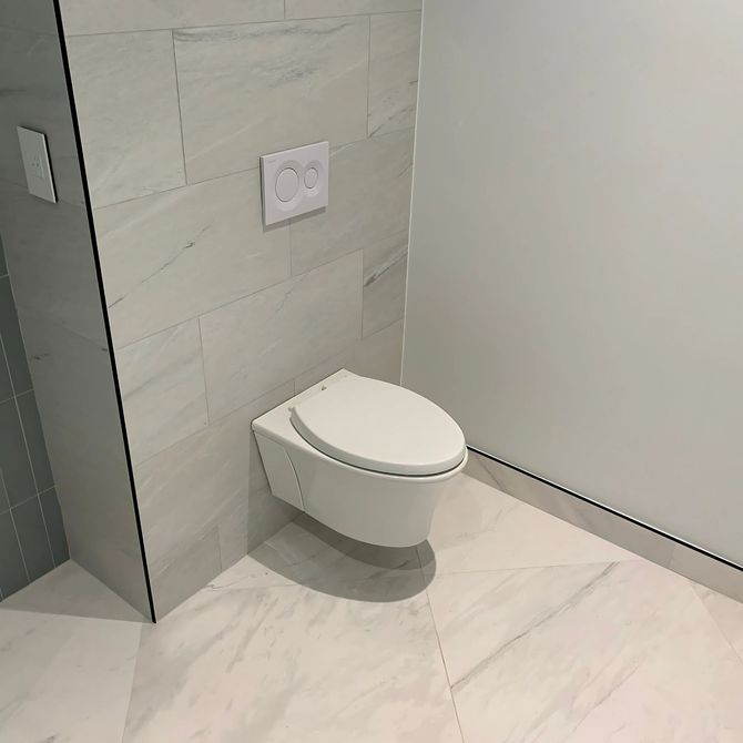 Blue Mountain Contractors LLC - A white toilet is mounted to the wall in a bathroom.