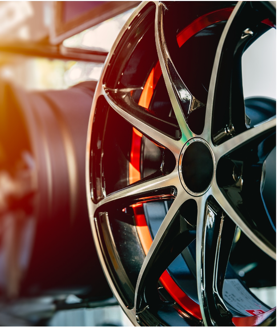Detalhe de uma roda de carro preta e prateada com detalhes em vermelho; outra roda ao fundo.