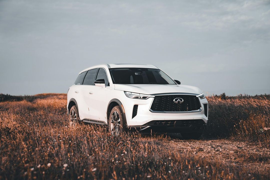 Um SUV Infiniti branco estacionado em uma estrada de terra em um campo gramado e seco sob um céu nublado.