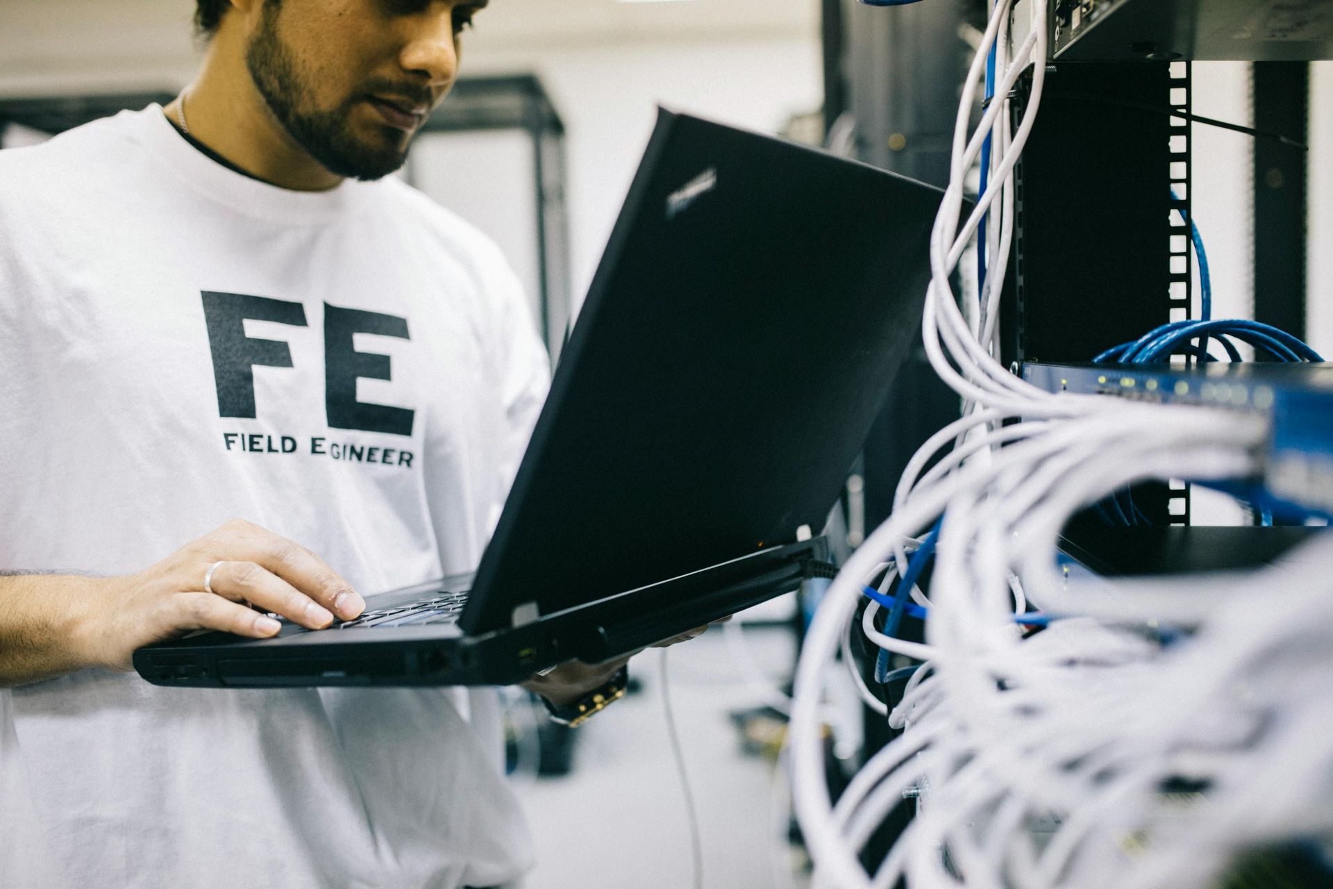 A man wearing a white shirt that says fe is working on a laptop