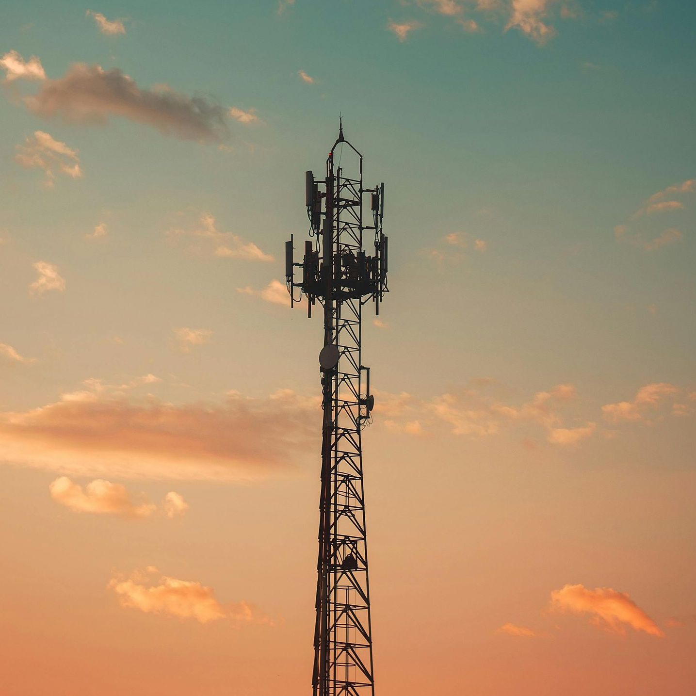 A telephone tower is silhouetted against a sunset sky