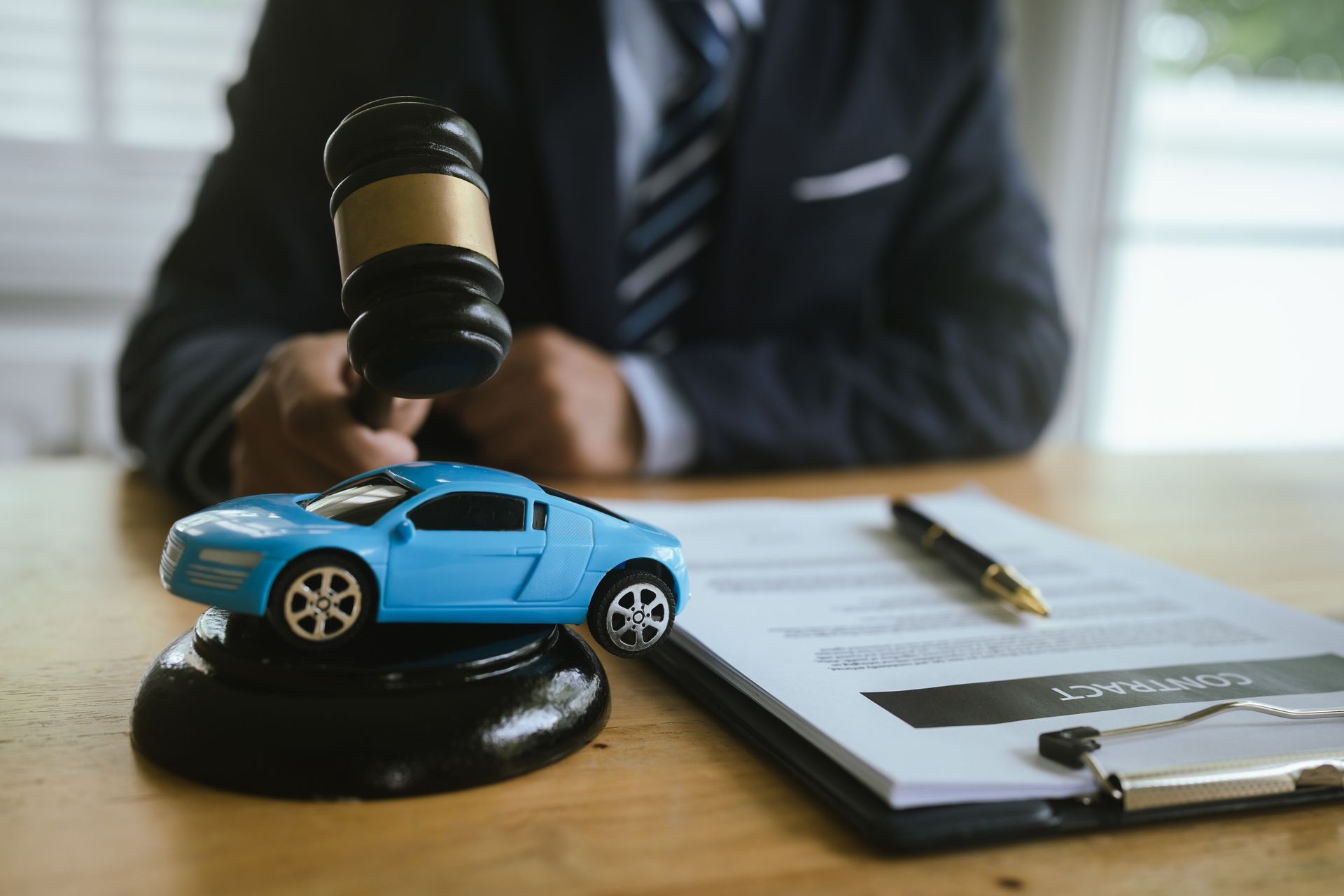 A gavel raised behind a blue toy car placed on a contract form on a desk.