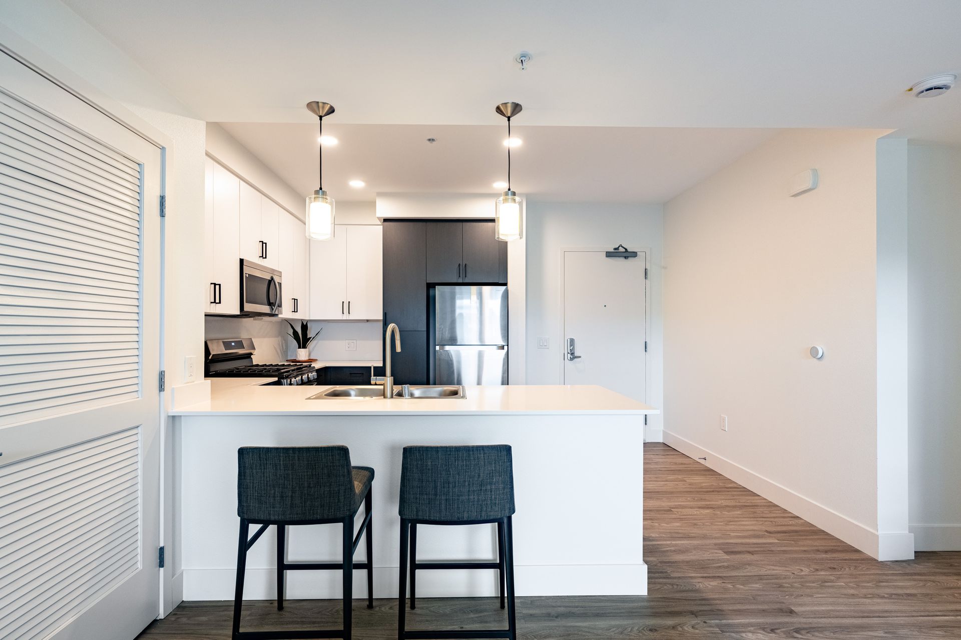 A kitchen with a stainless steel refrigerator , microwave , sink , and two stools.