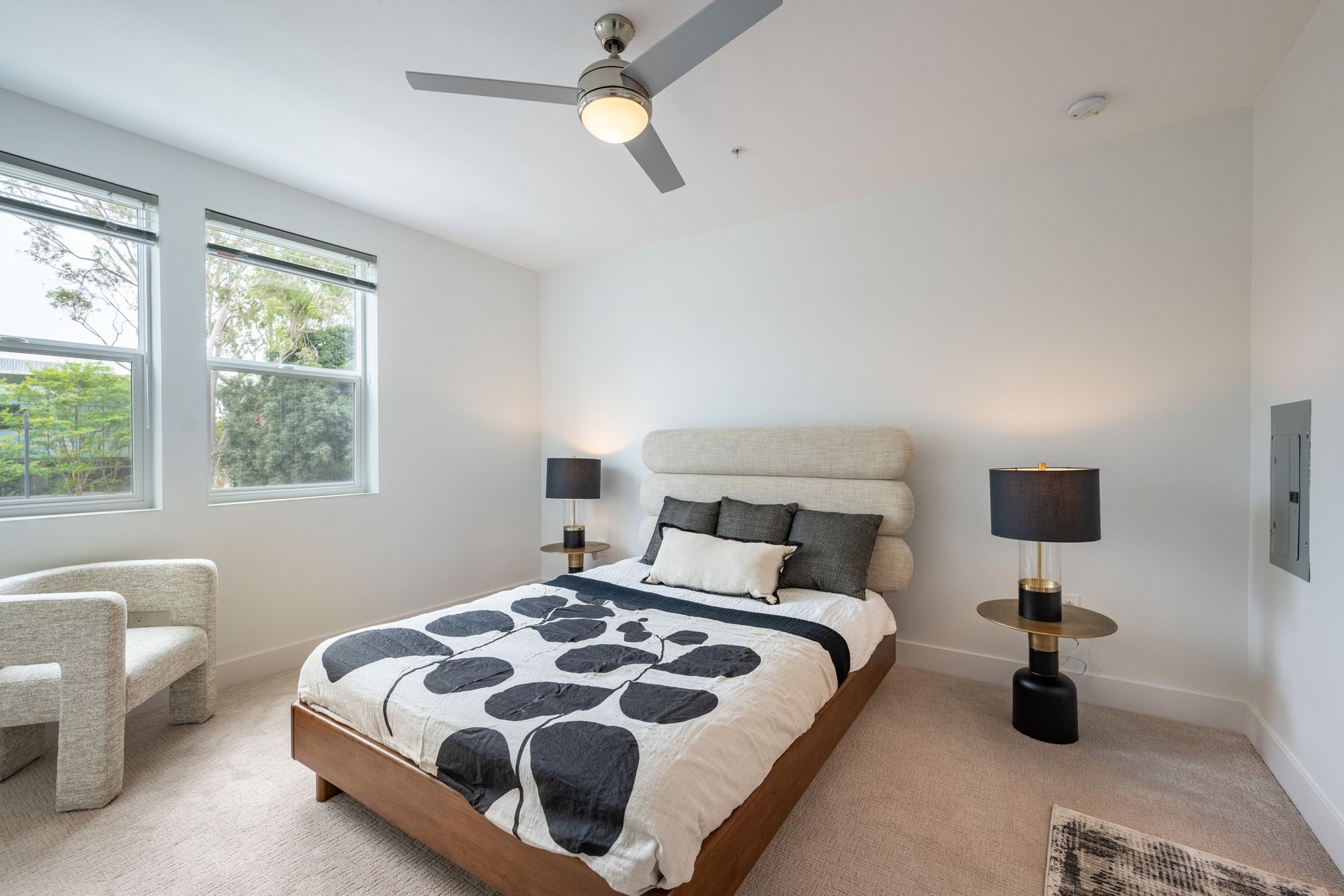 A bedroom with a bed , chair , lamps and a ceiling fan.