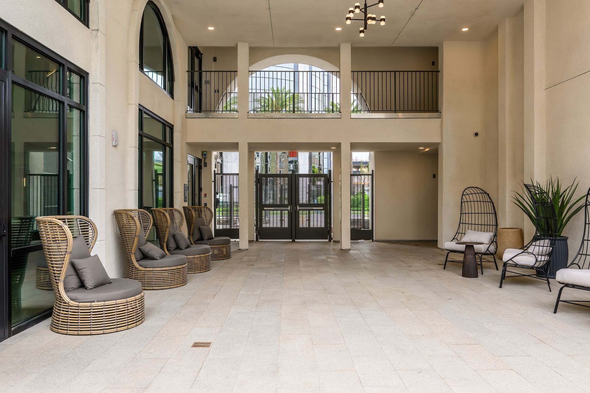 A well-lit outdoor lobby with seating, arched doorway, and a wrought iron balcony overhead.