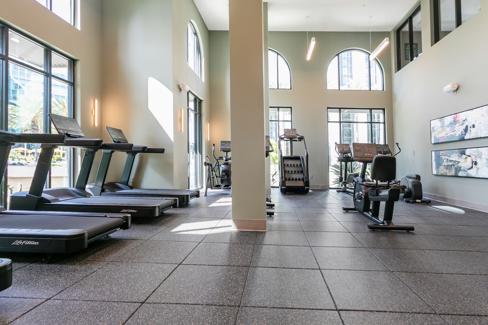 Gym interior with treadmills, weight machines, and large windows.