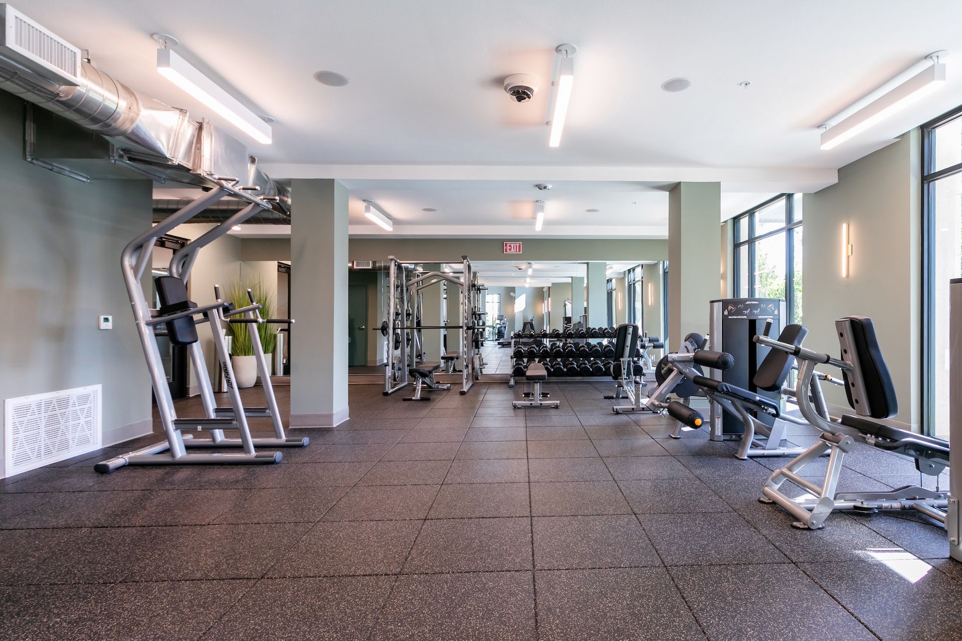 Gym interior with exercise machines, weights, and dark floor. Well-lit space.