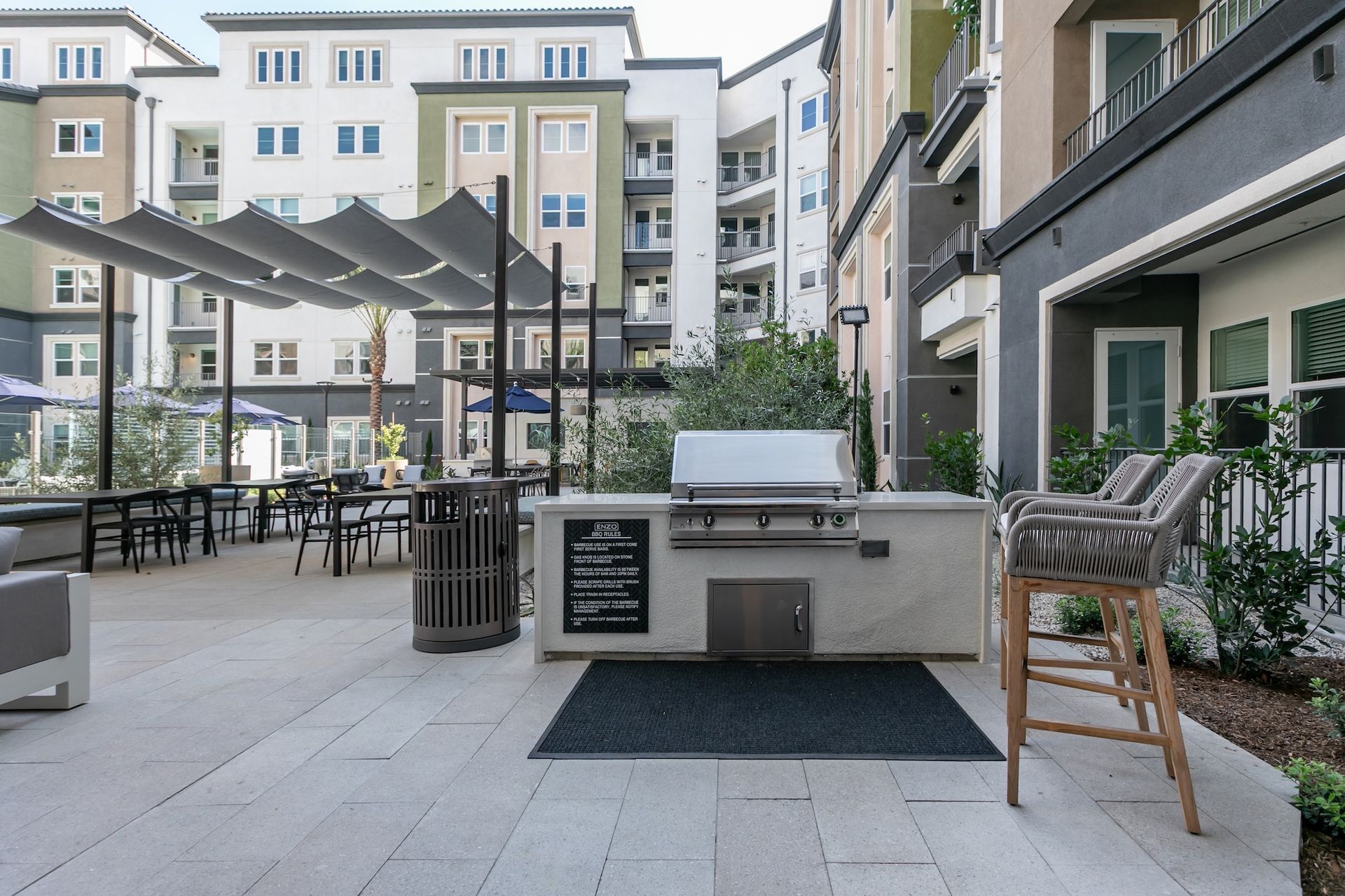 Outdoor grilling area with a built-in grill, tables, chairs, and multi-story apartment buildings.