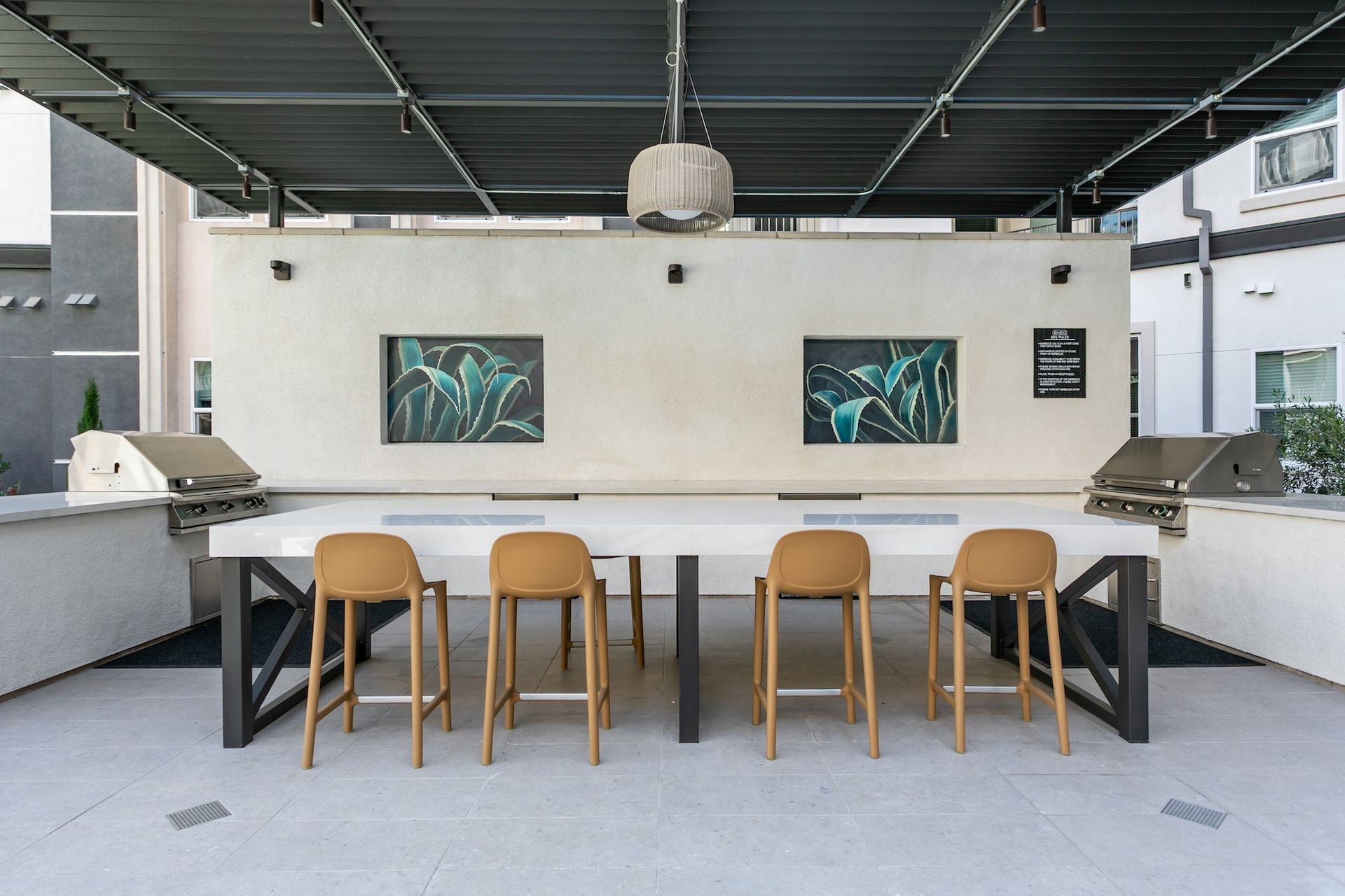 Outdoor grilling station with long table, stools, and grills.