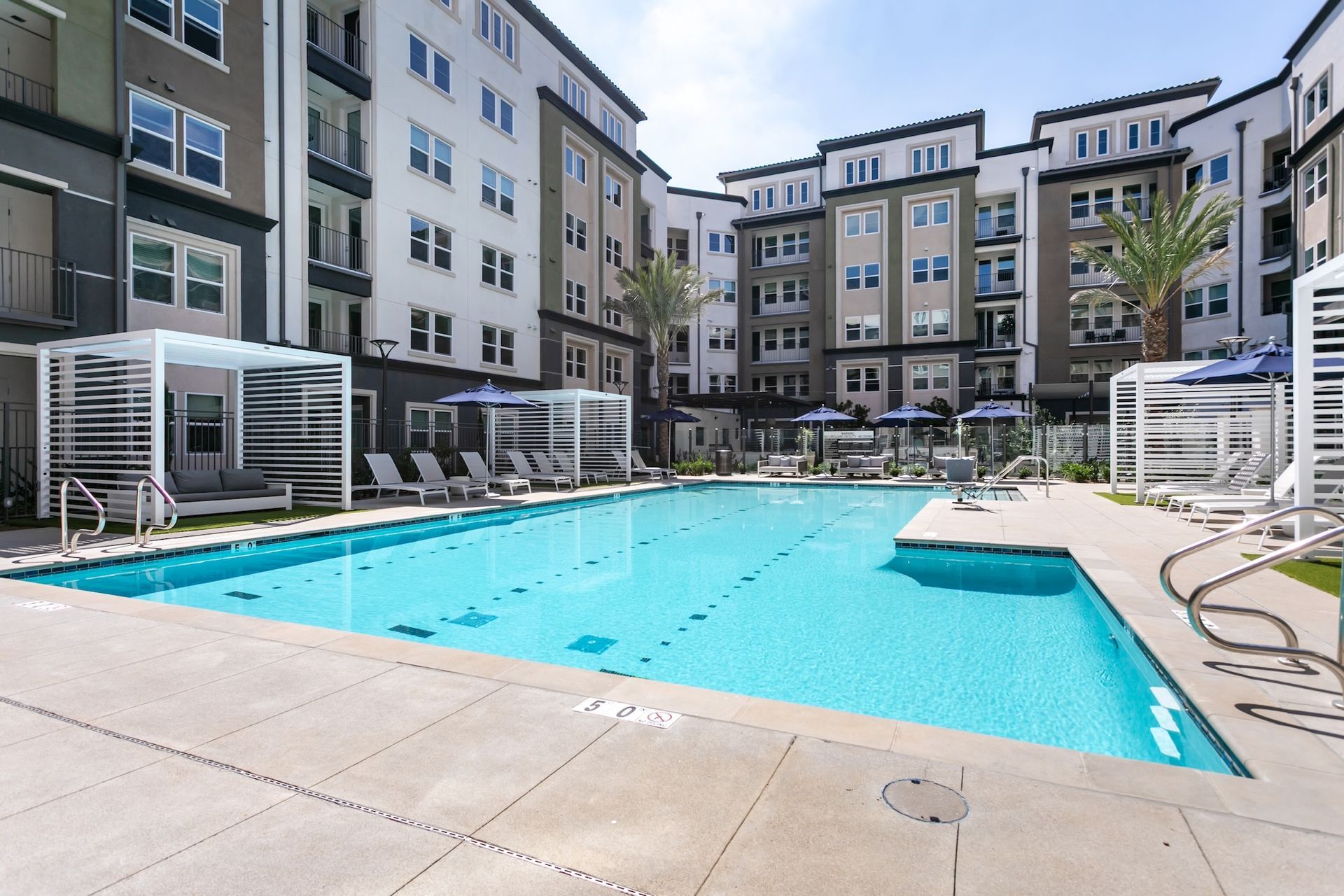 Swimming pool at an apartment complex with lounge chairs, cabanas, and multi-story buildings.