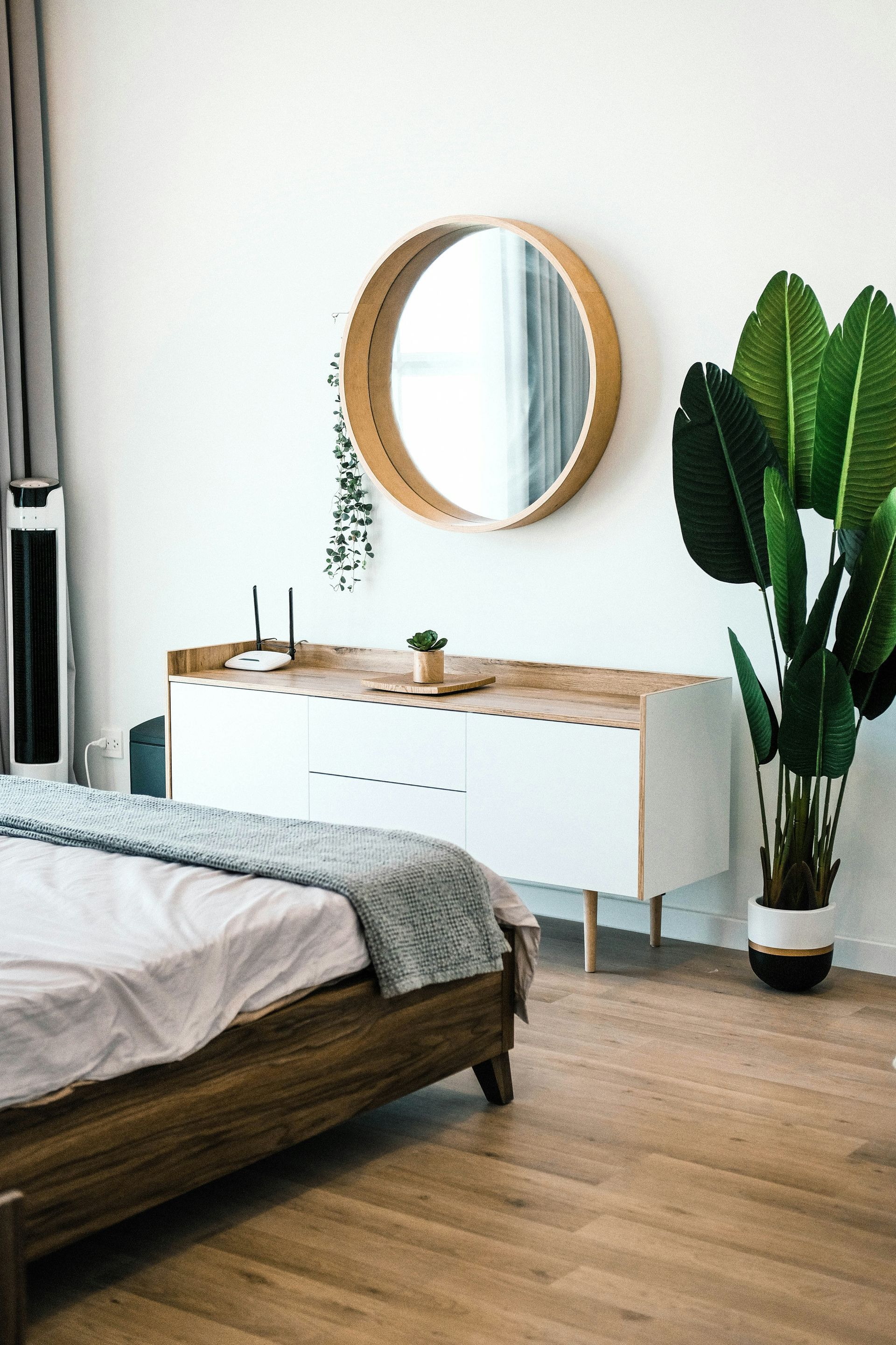 A bedroom with a bed , dresser , mirror and potted plant.