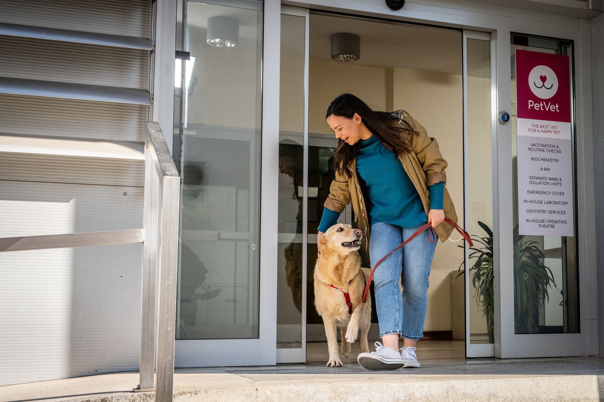 A smiling woman walks out of a local dog day care center with her Golden Retriever on a leash.