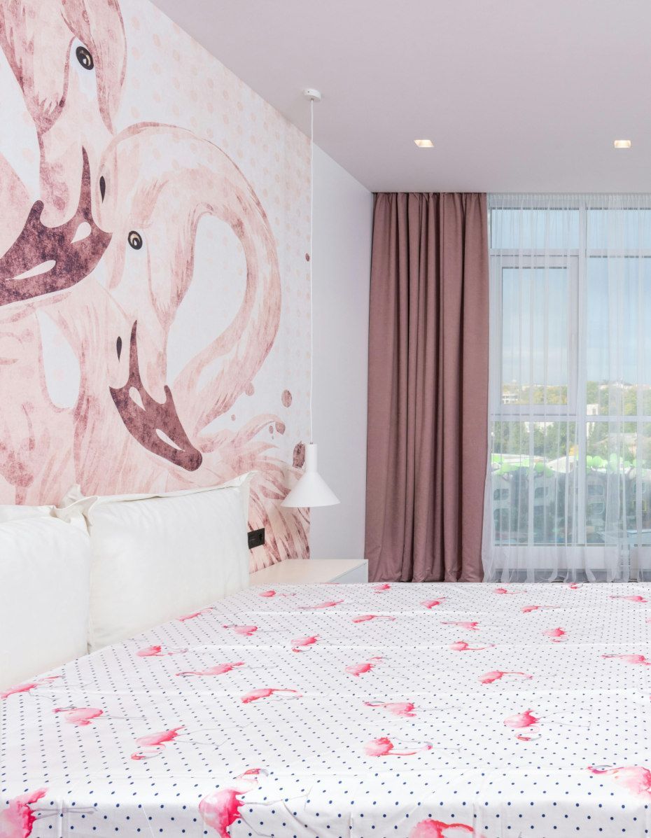Bedroom with flamingo mural, pink accents, polka dot bedspread, and window with drapes.