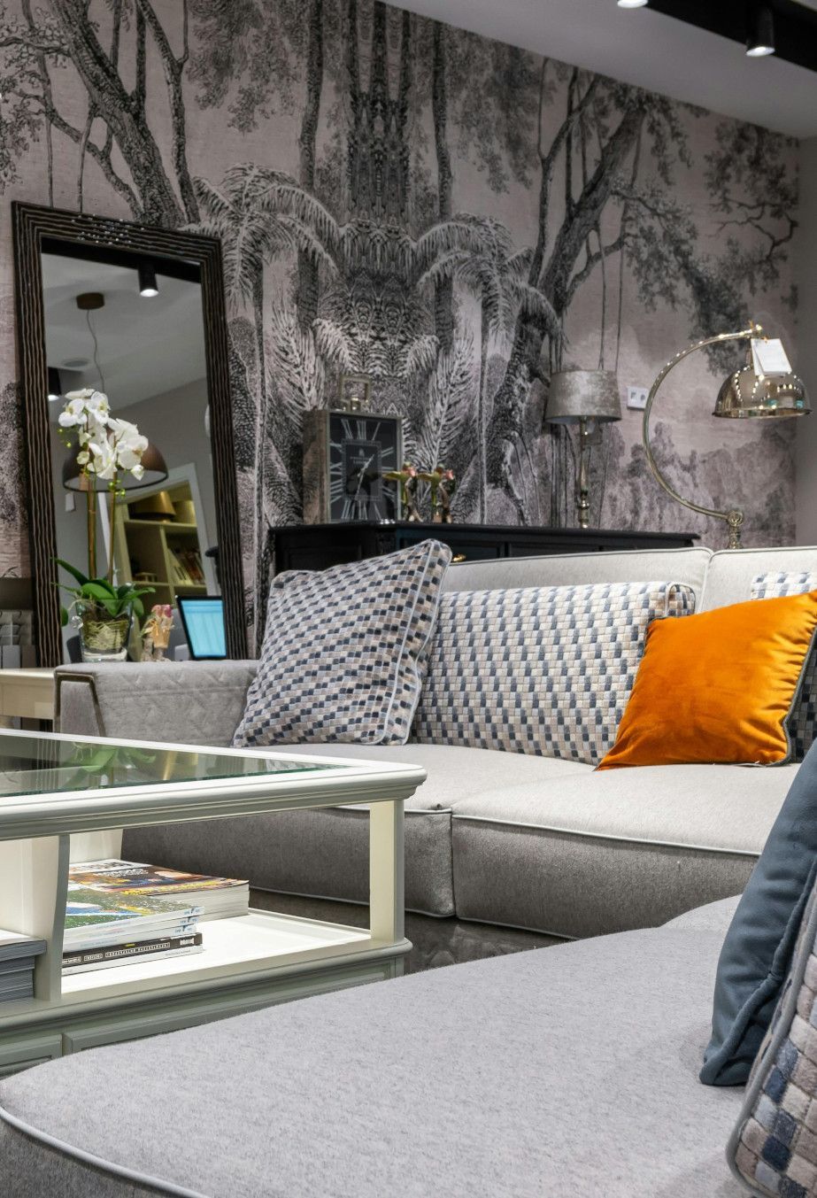 Living room with gray sofa, patterned pillows, mirror, coffee table, and forest mural wallpaper.